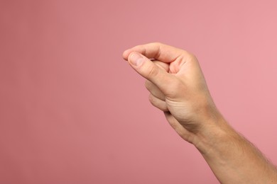 Photo of Man holding something in fingers on pink background, closeup. Space for text