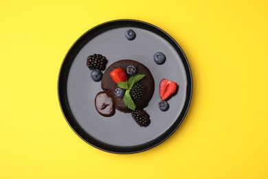 Photo of Plate with delicious chocolate fondant, berries and mint on yellow table, top view