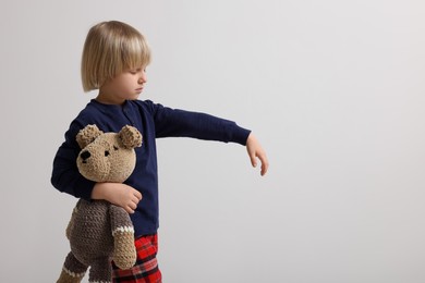 Boy in pajamas with toy bear sleepwalking on white background, space for text