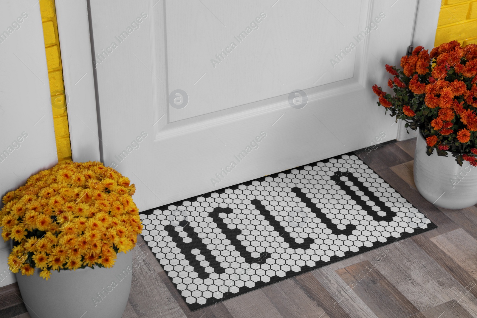 Photo of Stylish door mat with word Hello and beautiful flowers on wooden floor
