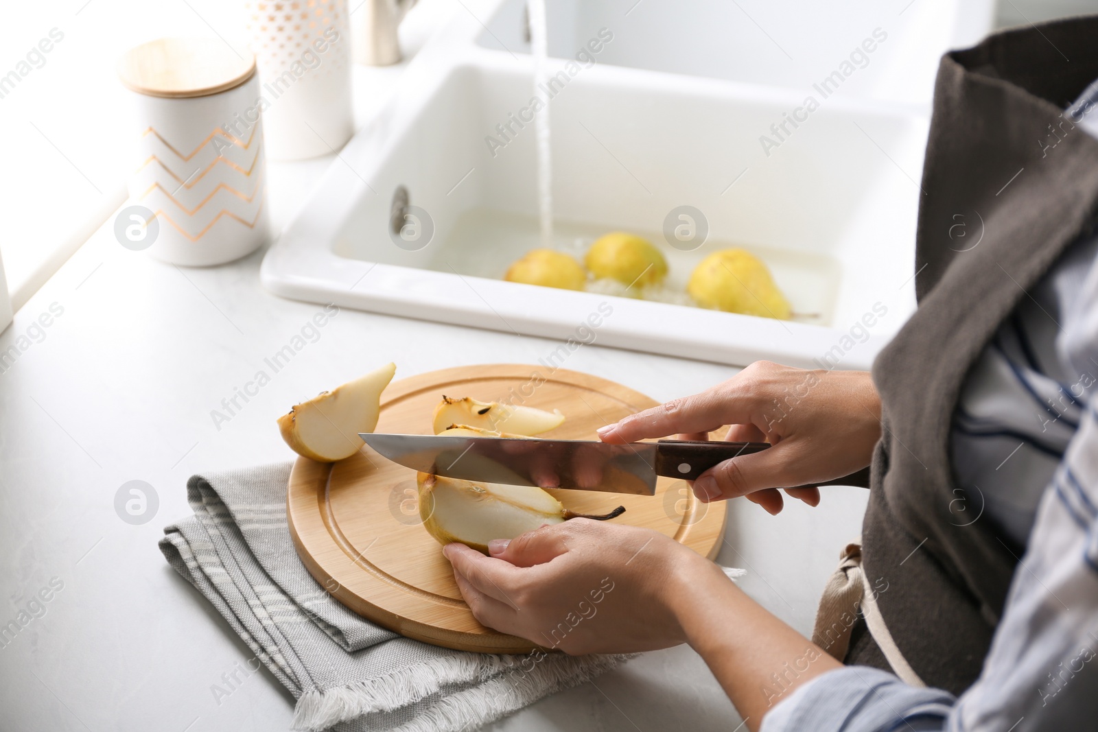 Photo of Woman cutting fresh ripe pear at table in kitchen, closeup