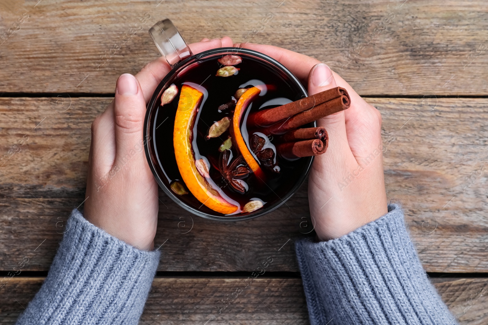 Photo of Woman with cup of mulled wine at wooden table, top view