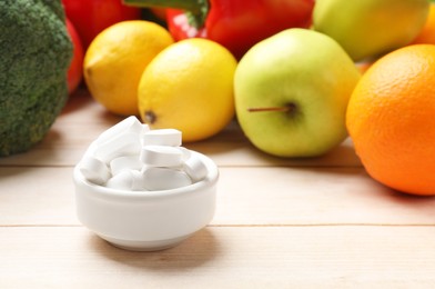 Photo of Dietary supplements. Bowl with pills near food products on light wooden table, closeup