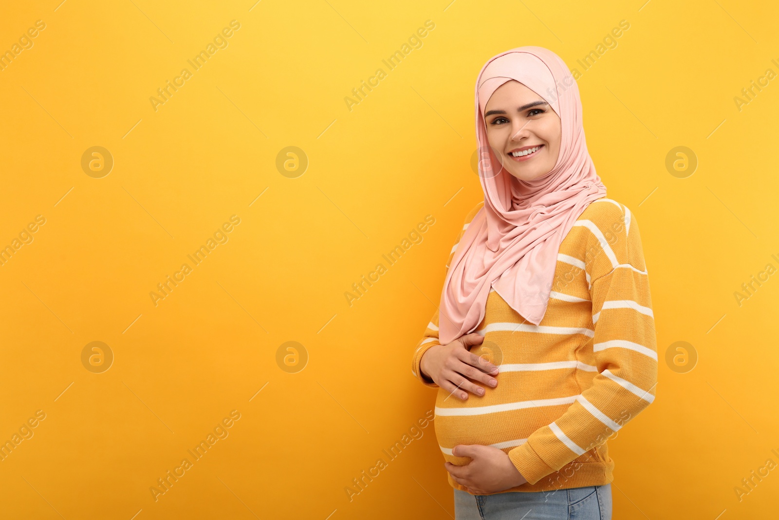 Photo of Portrait of pregnant Muslim woman in hijab on orange background, space for text