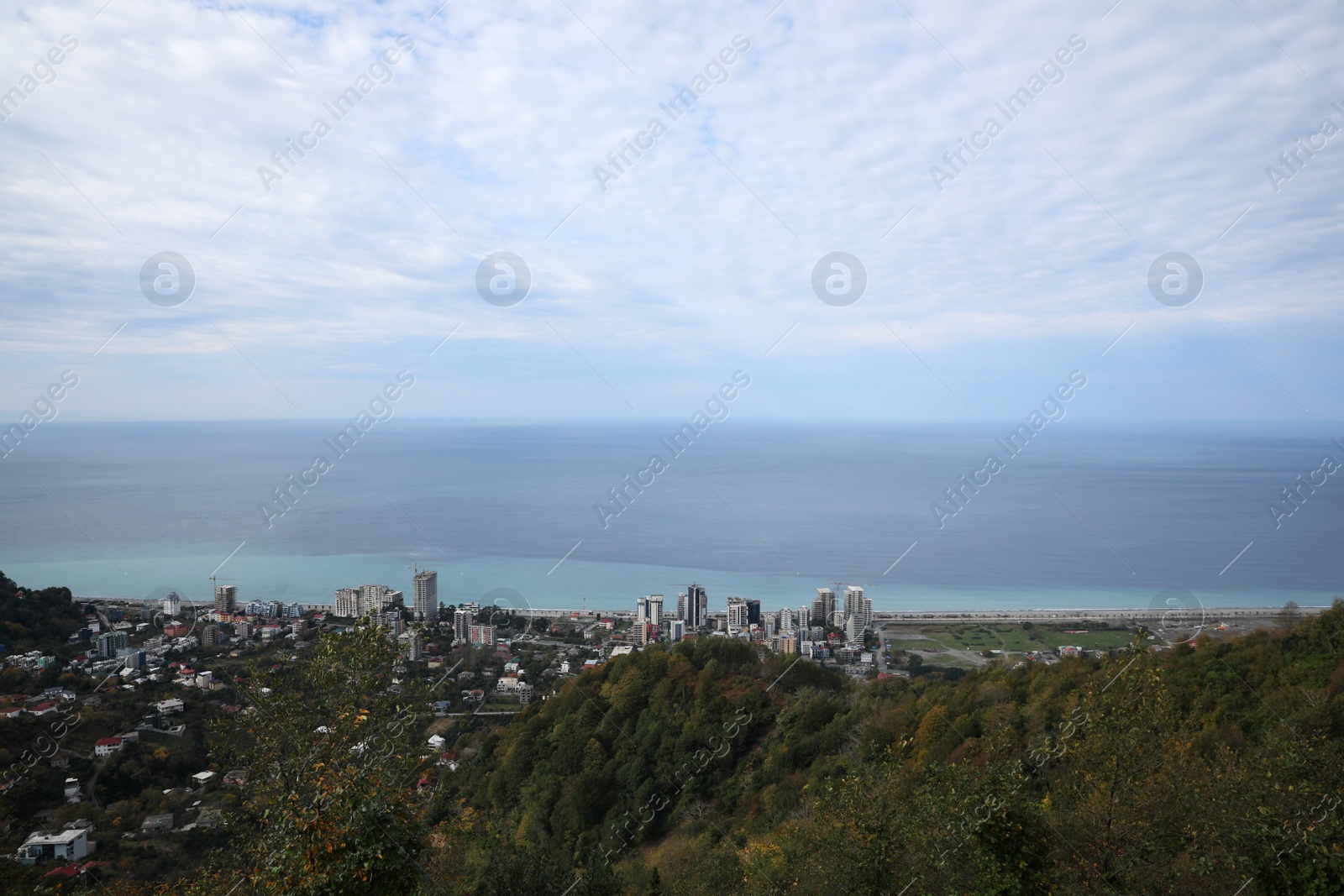 Photo of Picturesque view of city, green trees and beautiful sea under cloudy sky