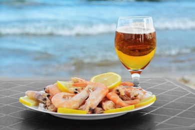 Photo of Cold beer in glass and shrimps served with lemon on beach