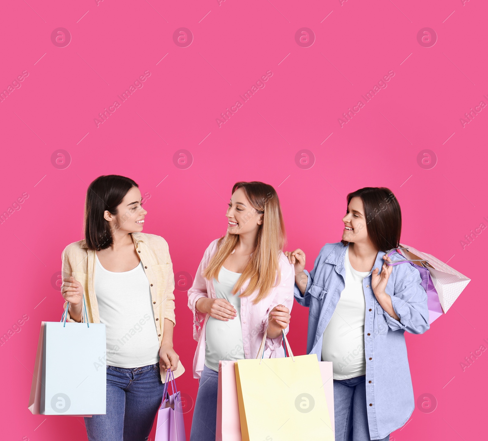 Photo of Happy pregnant women with shopping bags on pink background