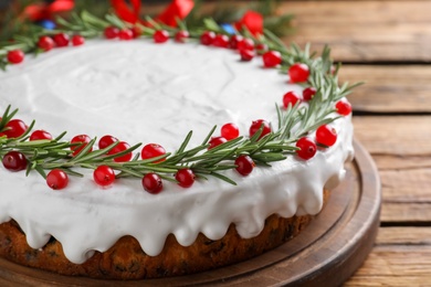 Photo of Traditional Christmas cake decorated with rosemary and cranberries on wooden table, closeup