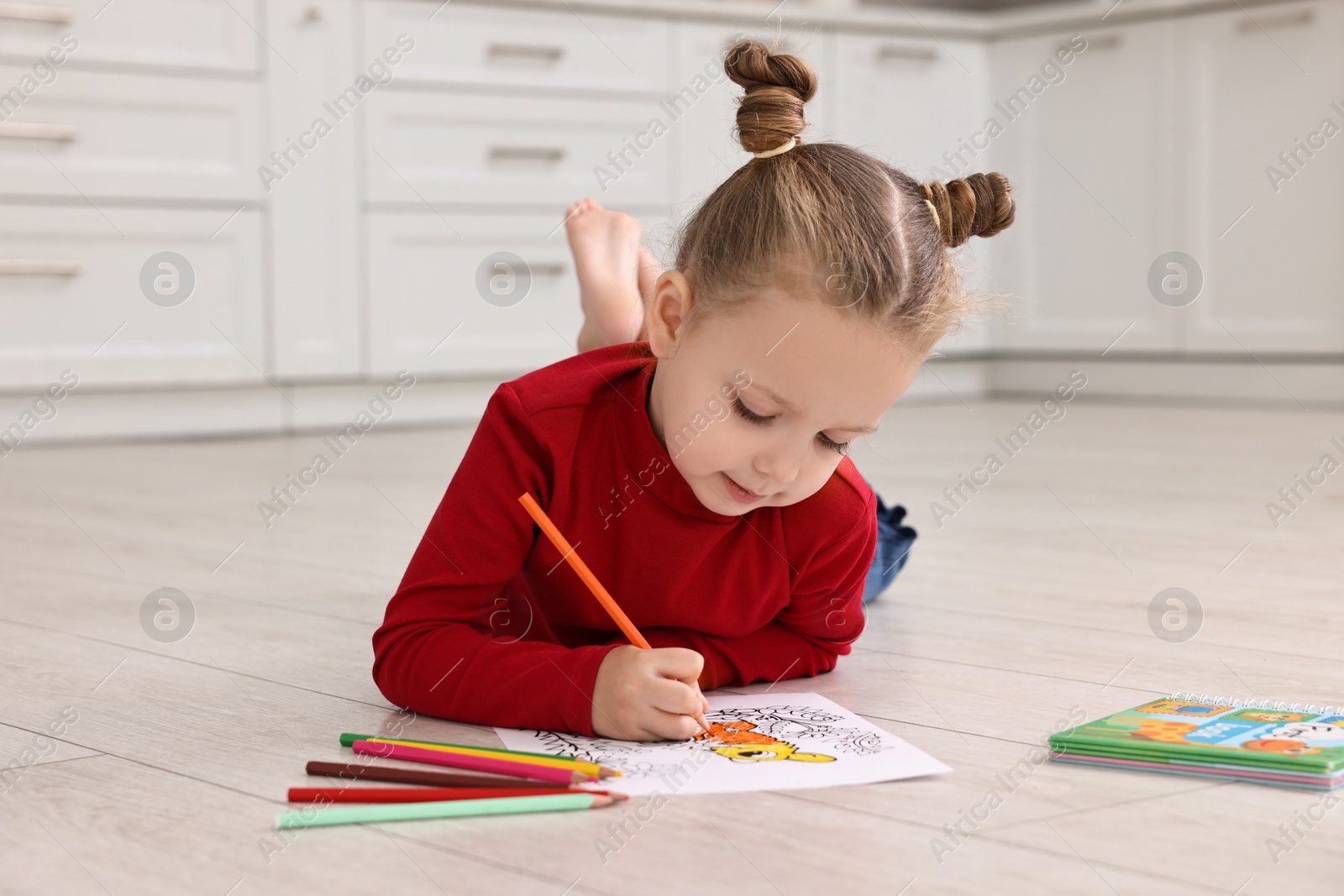 Photo of Cute little girl coloring on warm floor in kitchen. Heating system