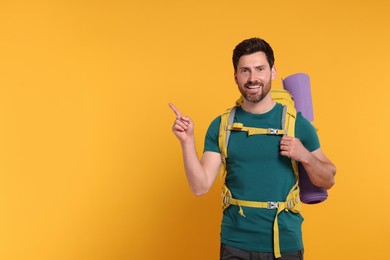 Photo of Happy man with backpack pointing at something on orange background, space for text. Active tourism