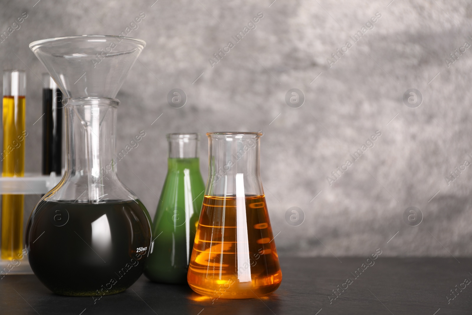 Photo of Flasks and test tubes with different types of oil on grey table, closeup. Space for text