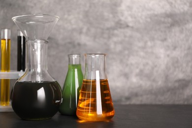 Flasks and test tubes with different types of oil on grey table, closeup. Space for text