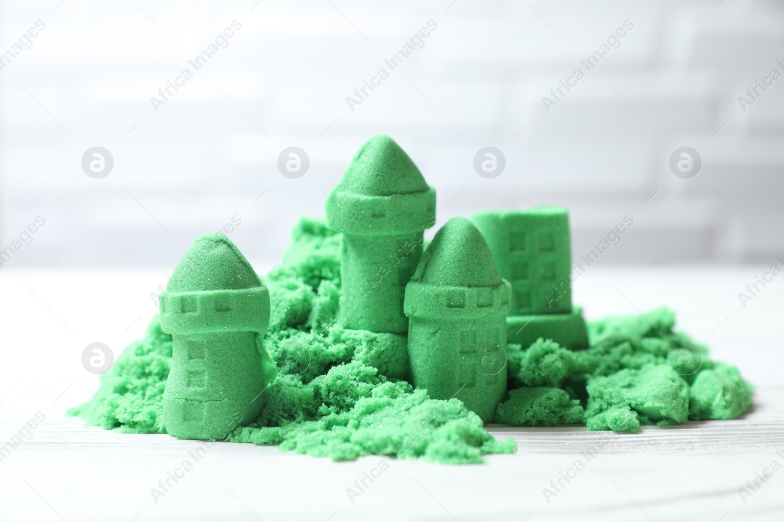 Photo of Castle figures made of green kinetic sand on white table, closeup