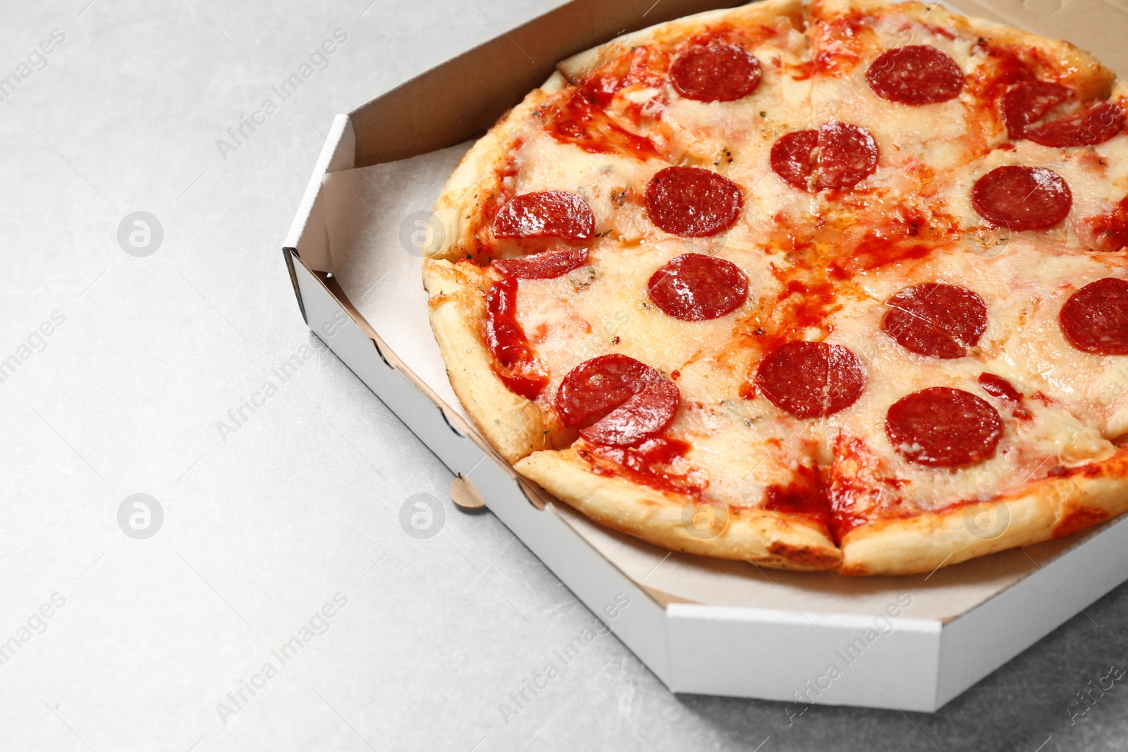 Photo of Hot delicious pepperoni pizza in cardboard box on light grey table