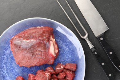 Photo of Plate with pieces of raw beef meat, knife and fork on grey textured table, flat lay