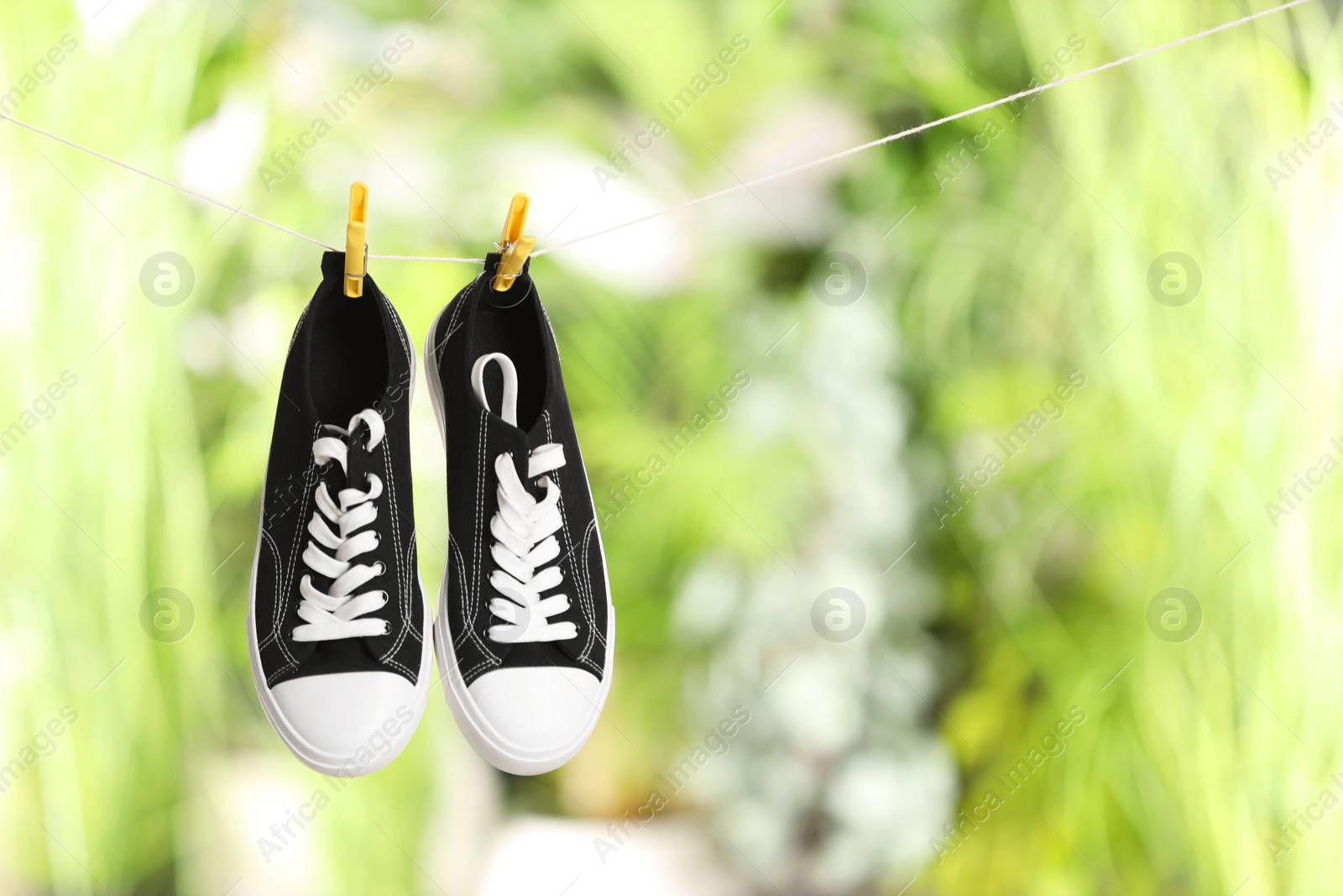 Photo of Stylish sneakers drying on washing line against blurred background, space for text