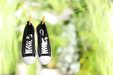 Photo of Stylish sneakers drying on washing line against blurred background, space for text