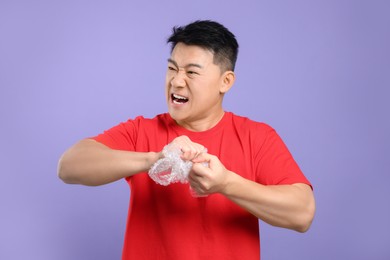 Photo of Emotional asian man with bubble wrap on purple background
