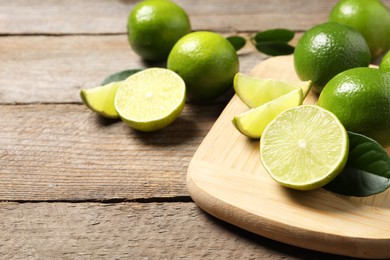 Photo of Whole and cut fresh limes on wooden table. Space for text