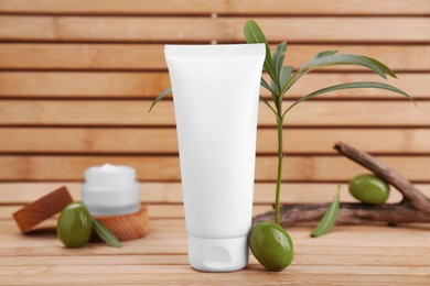 Tube of natural cream, olives and leaves on wooden table