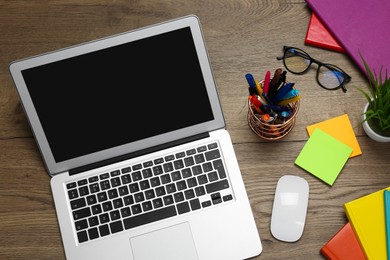 Modern laptop, glasses and office stationery on wooden table, flat lay. Distance learning