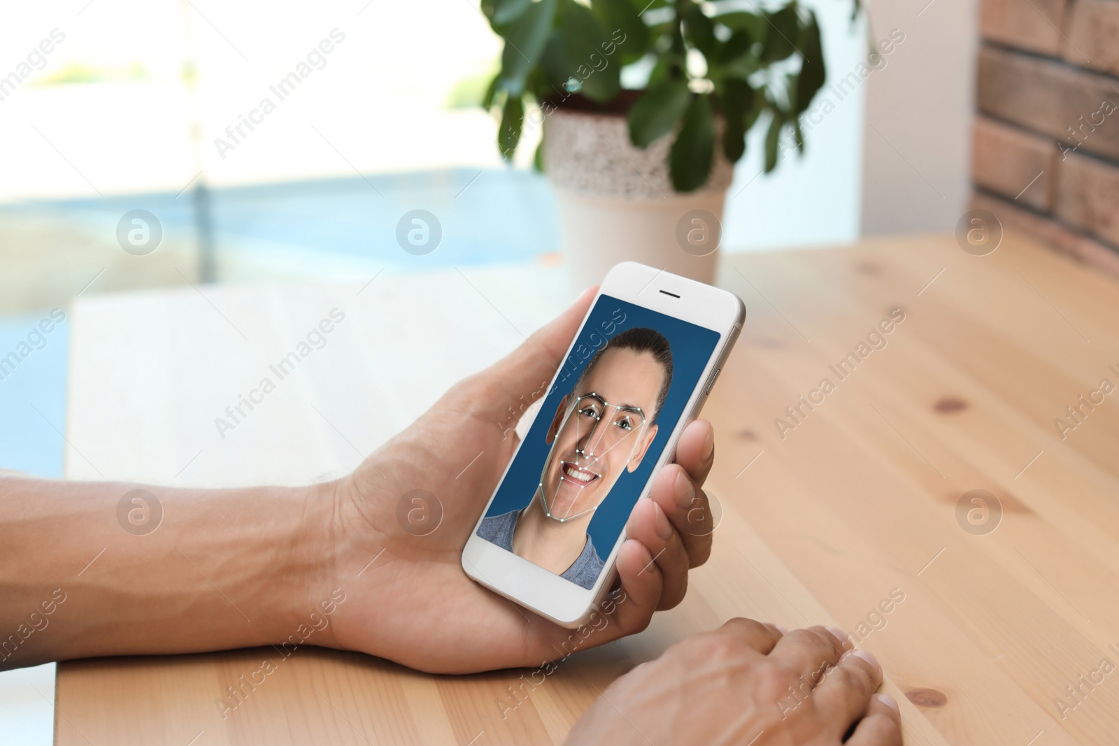 Image of Man using smartphone with facial recognition system at table indoors, closeup. Biometric verification