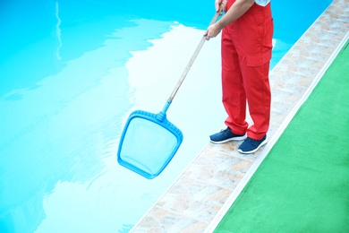 Photo of Male worker cleaning outdoor pool with scoop net