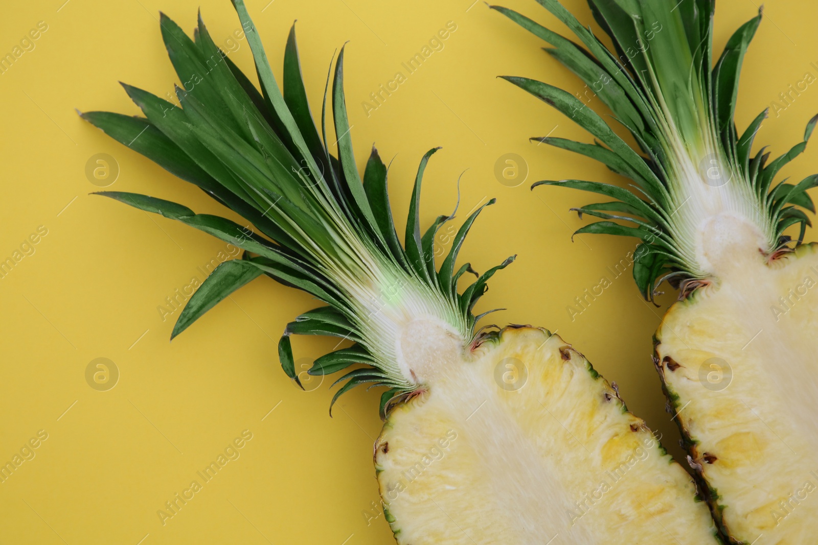 Photo of Halves of ripe pineapple on yellow background, flat lay