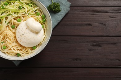Photo of Bowl of delicious pasta with burrata, peas and zucchini on wooden table, top view. Space for text