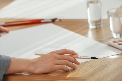 Photo of Man with brushes and blank papers at wooden table, closeup. Watercolor artwork