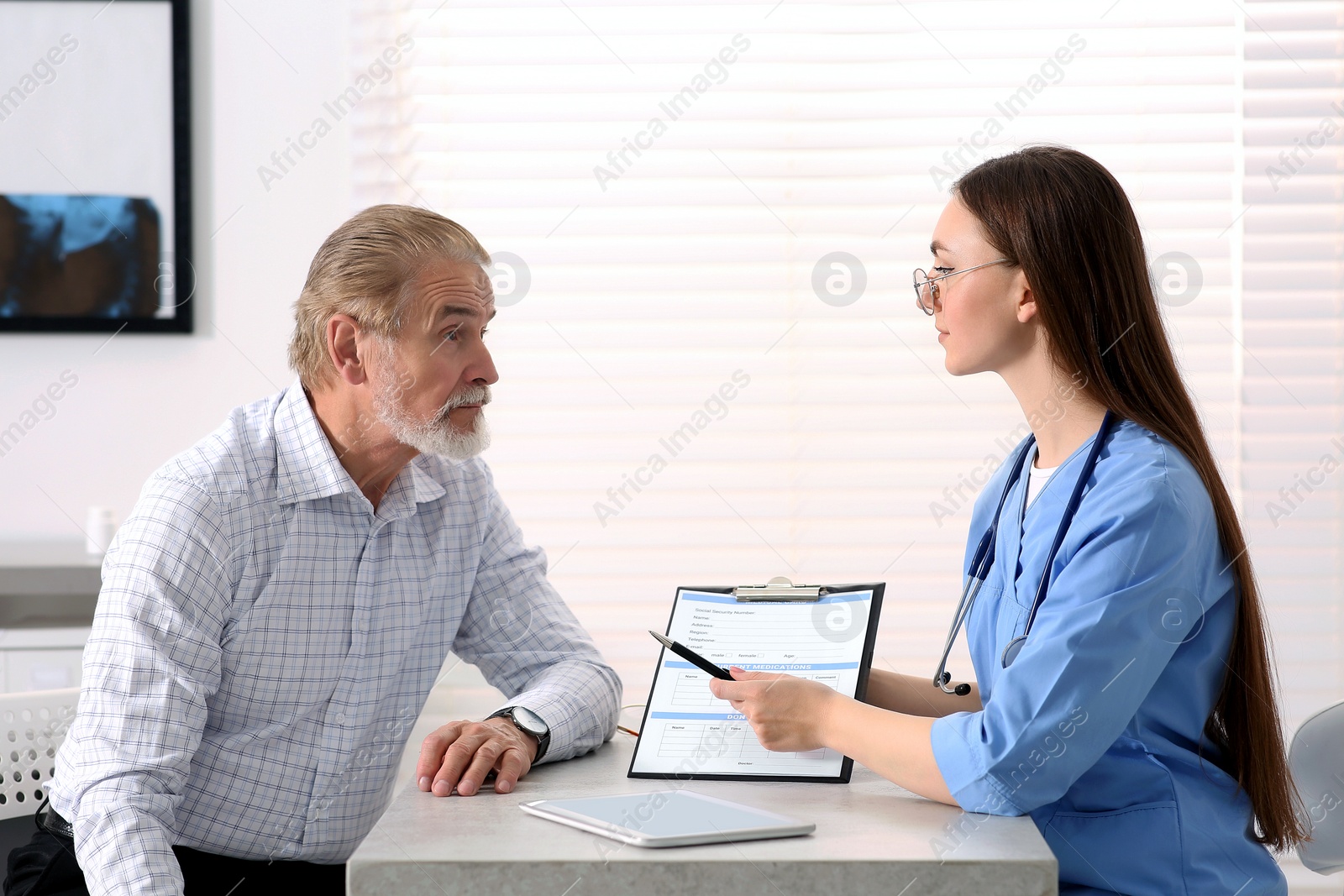 Photo of Doctor showing medical card to patient at table in clinic