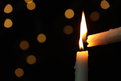 Photo of Lighting candle from another one against blurred lights in darkness, closeup. Space for text