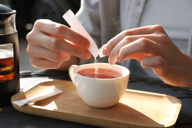 Woman adding sugar into cup of tea at table, closeup