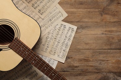 Photo of Paper sheets with music notes and acoustic guitar on wooden table, top view. Space for text