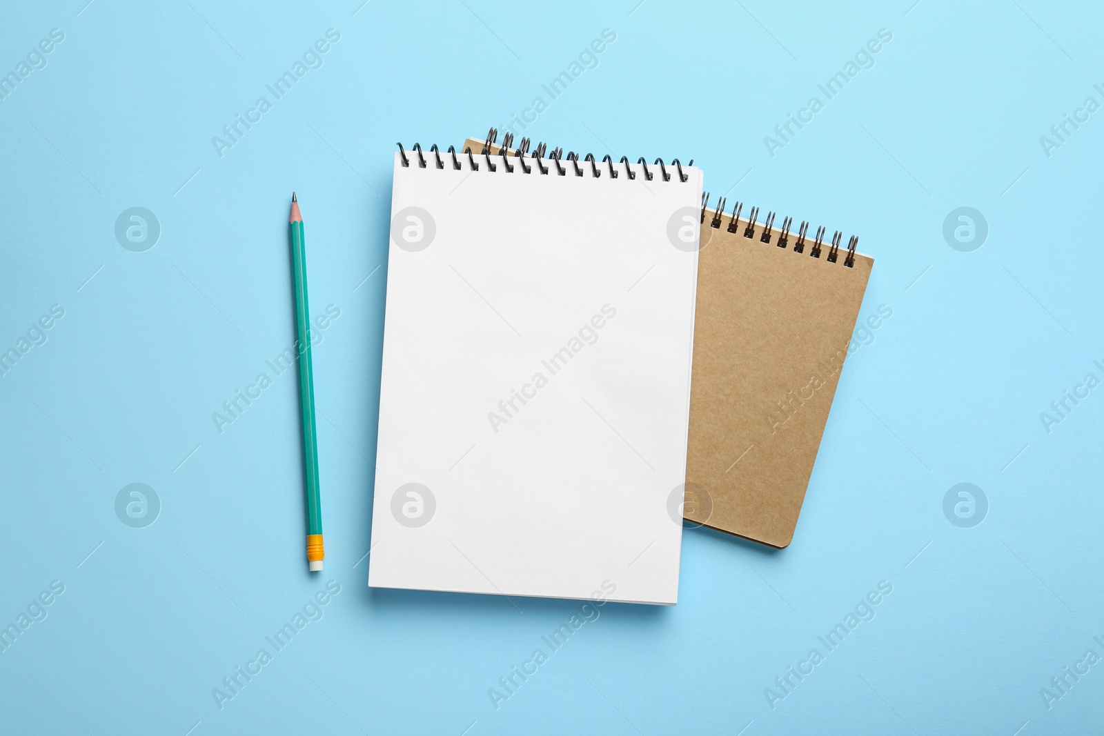 Photo of Notebooks and pencil on light blue background, top view
