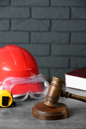 Construction and land law concepts. Gavel, hard hat, protective goggles and measuring tape on gray table against brick wall