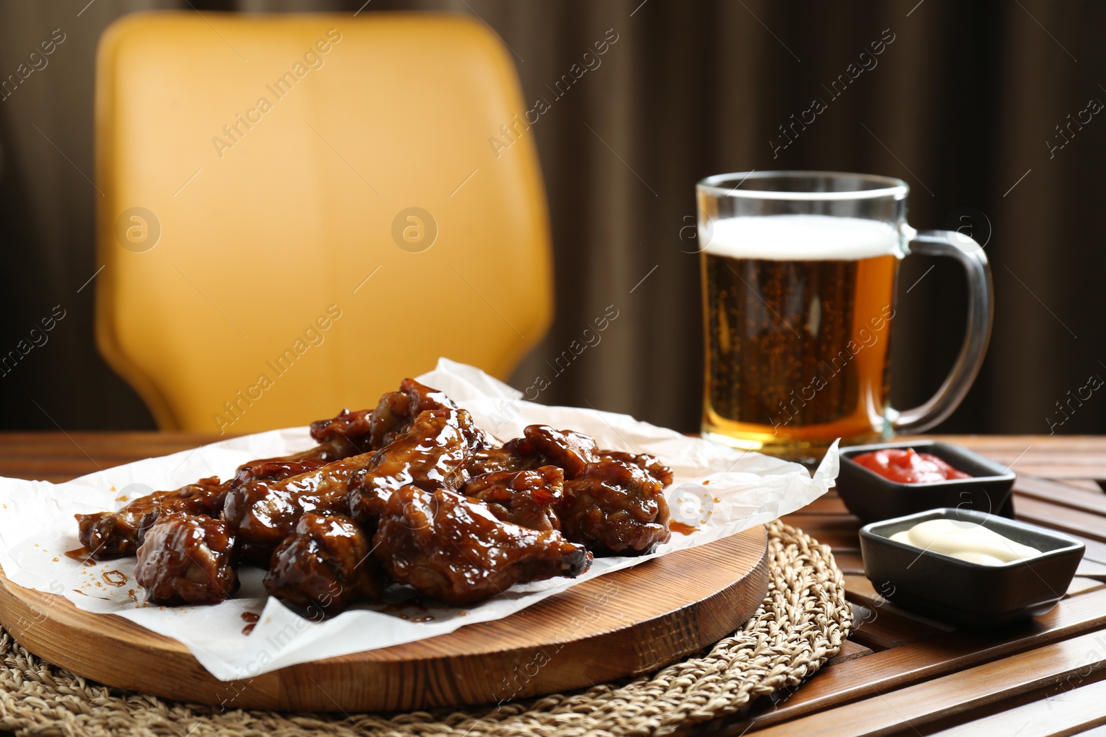 Photo of Tasty chicken wings, sauces and mug of beer on wooden table, space for text. Delicious snack