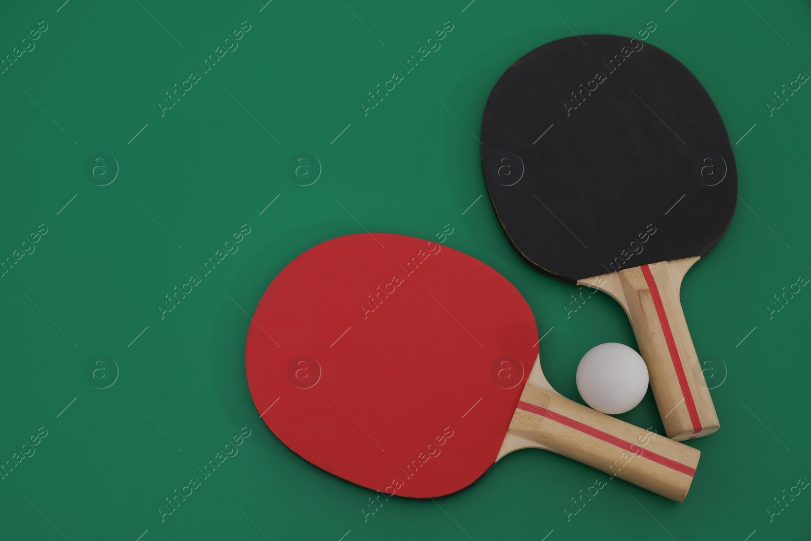 Photo of Ping pong rackets and ball on green background, flat lay. Space for text