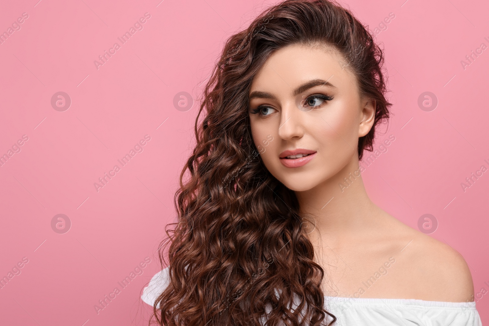 Photo of Beautiful young woman with long curly brown hair on pink background, space for text