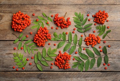 Photo of Fresh ripe rowan berries and green leaves on wooden table, flat lay