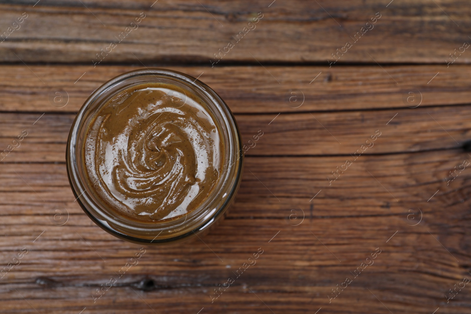 Photo of Tasty nut paste in jar on wooden table, top view. Space for text