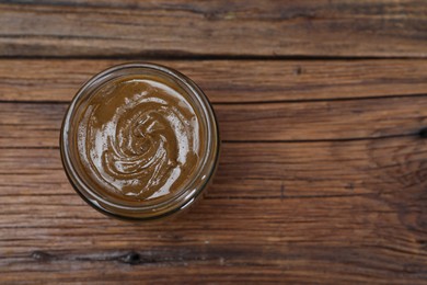 Photo of Tasty nut paste in jar on wooden table, top view. Space for text