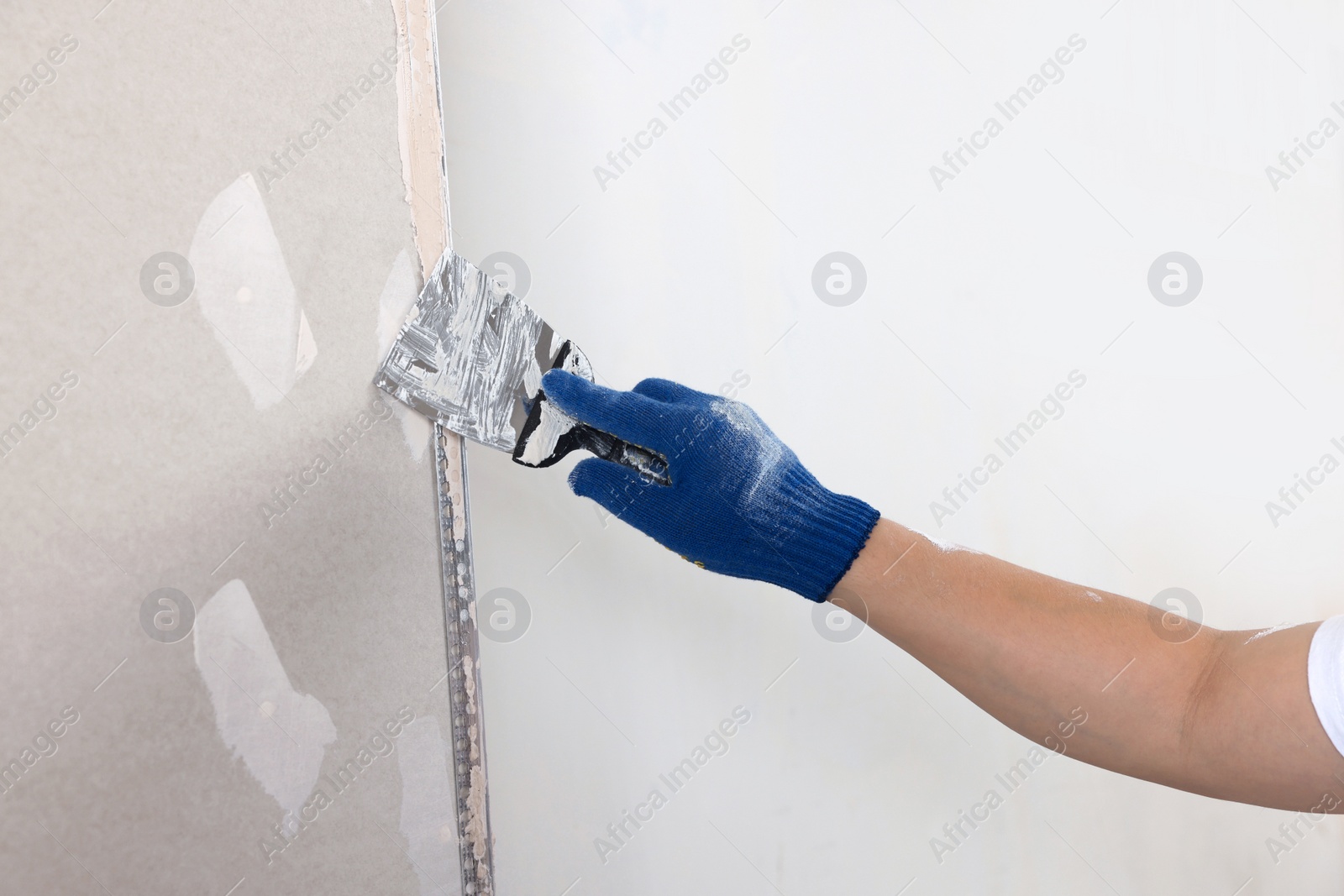 Photo of Man plastering wall with putty knife indoors, closeup. Home renovation