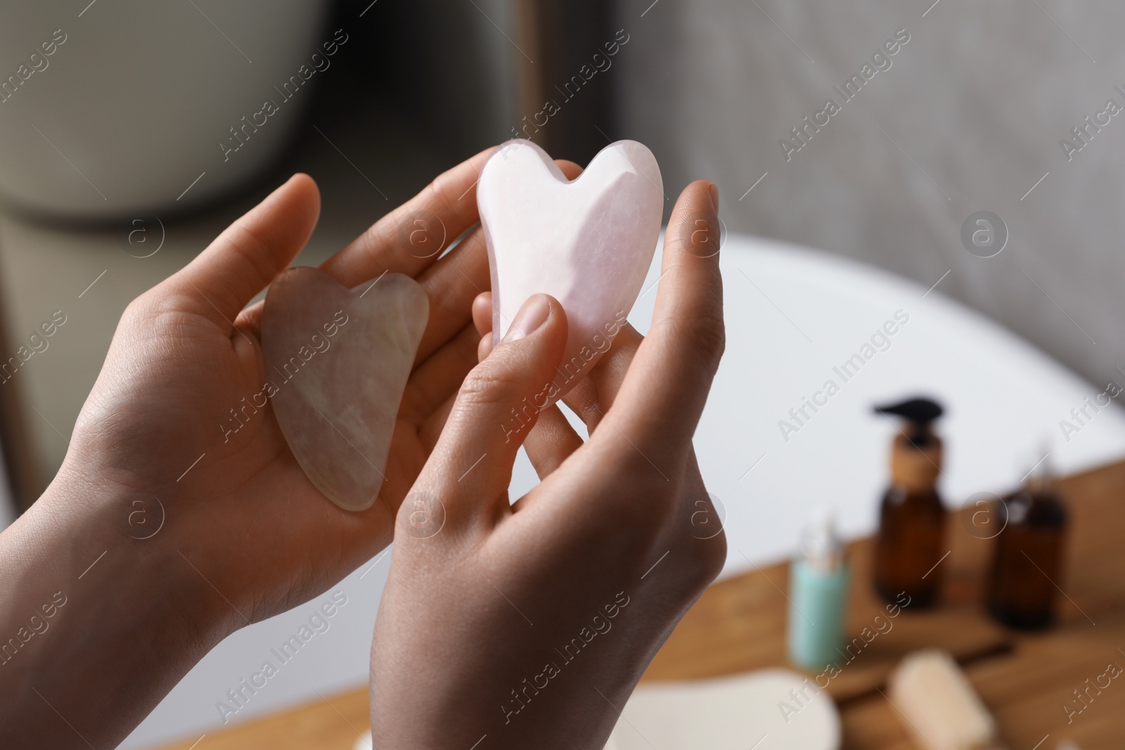 Photo of Woman holding jade and rose quartz gua sha tools in bathroom, closeup