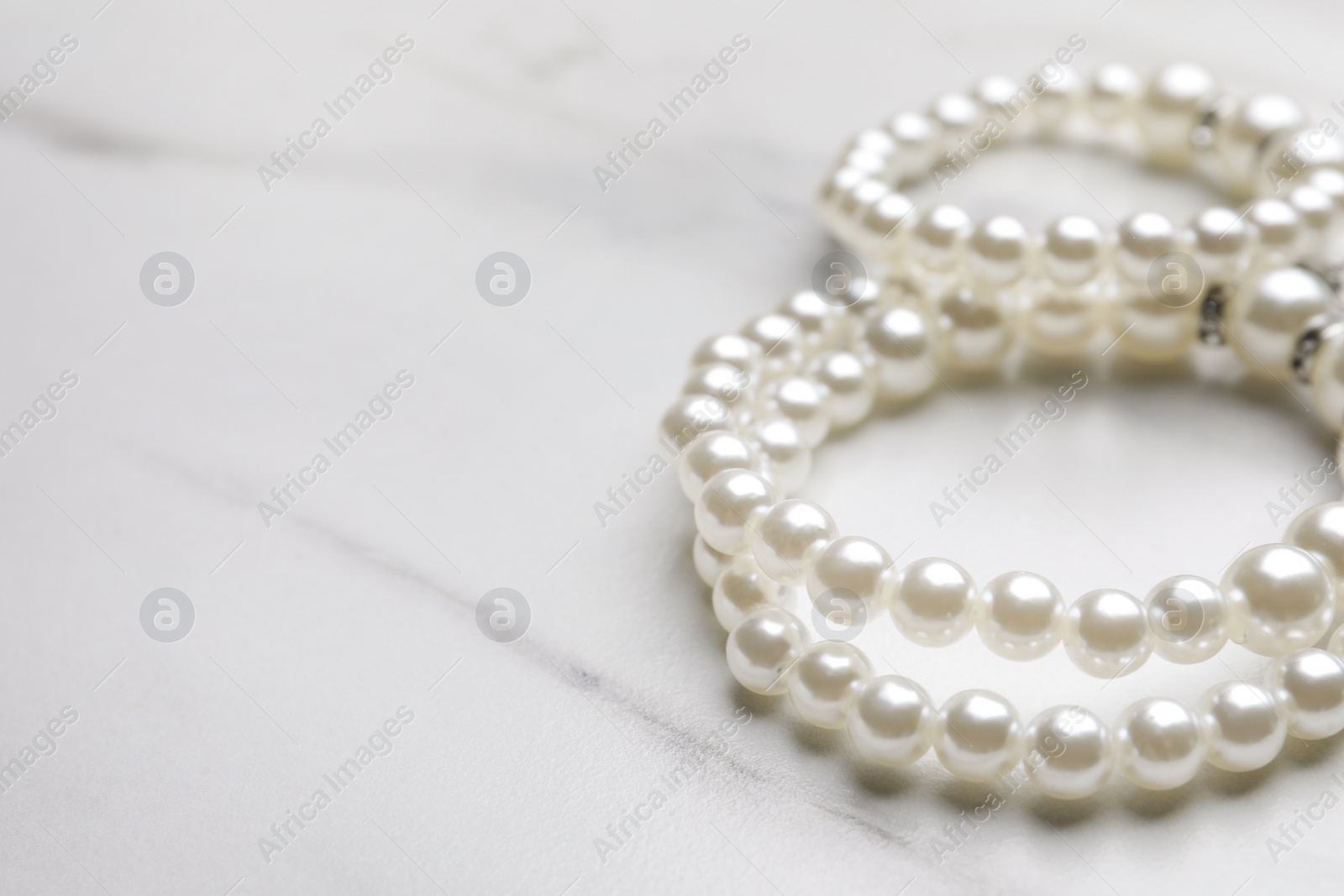 Photo of Elegant pearl bracelets on white marble table, closeup. Space for text