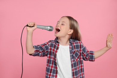 Photo of Cute little girl with microphone singing on pink background