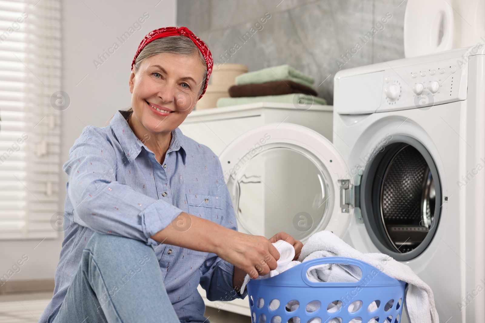 Photo of Happy housewife with laundry basket near washing machine at home