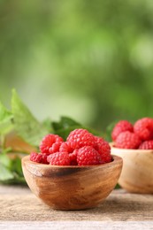 Tasty ripe raspberries in bowl on wooden table outdoors, space for text