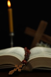 Photo of Wooden cross, rosary beads, Bible and church candle on table, closeup