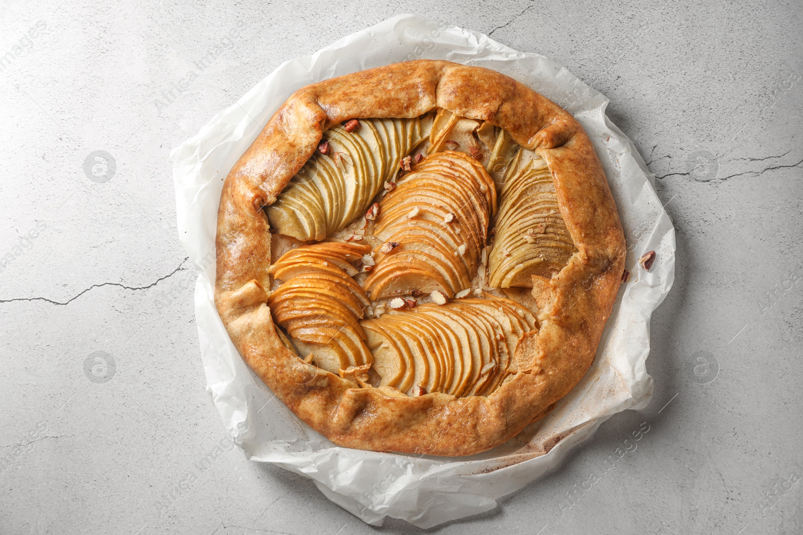 Photo of Delicious apple galette with pecans on light gray textured table, top view